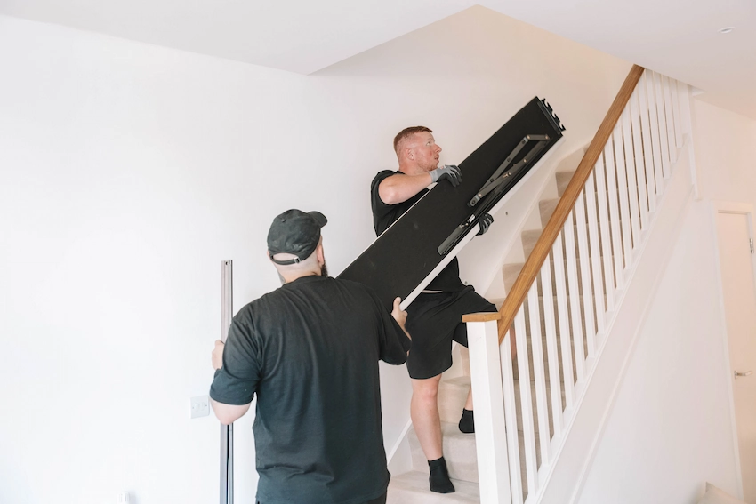 Two ShiftMate movers carefully carrying furniture upstairs during a house move