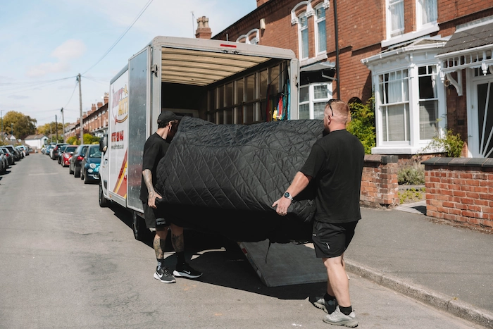 Two ShiftMate movers loading a covered furniture into a van
