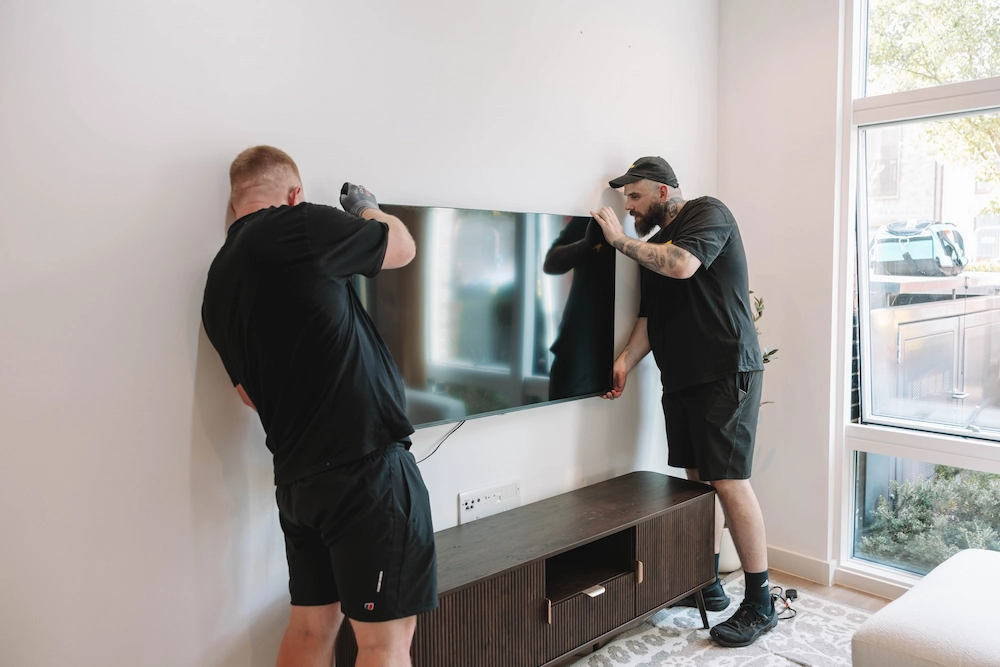Two ShiftMate movers carefully positioning a television above a media unit