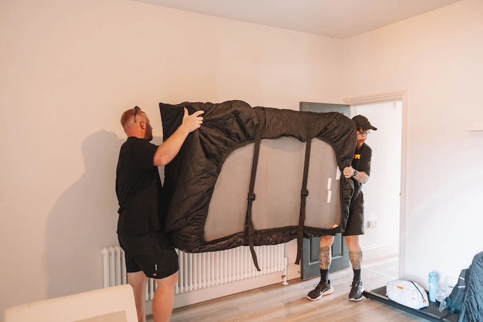 ShiftMate movers carefully lifting furniture secured inside a padded cover
