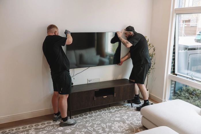 Two ShiftMate movers carefully positioning a television above a media unit