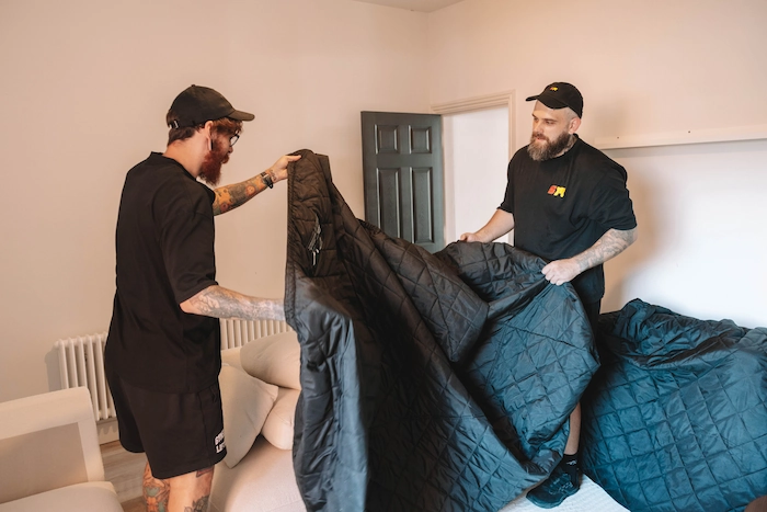 Two ShiftMate movers preparing a padded cover to protect furniture