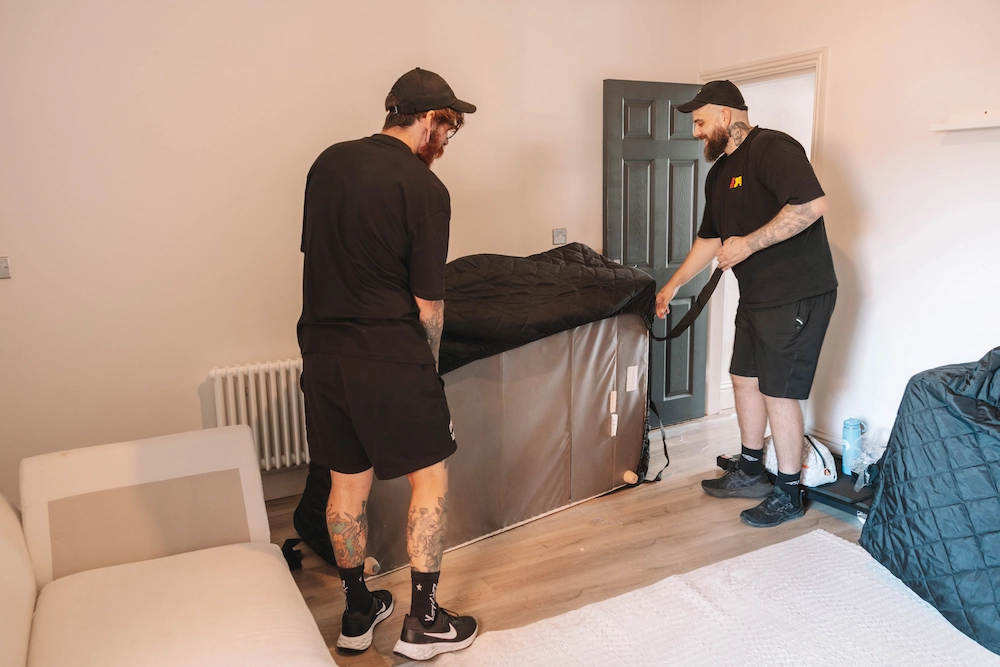 Two ShiftMate movers fitting a padded protective cover around furniture inside a home