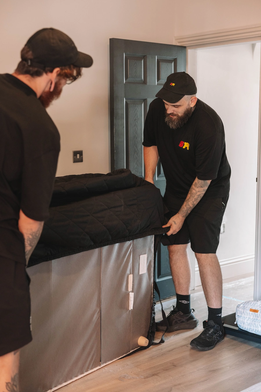 Two ShiftMate movers using a padded cover to protect furniture inside a home