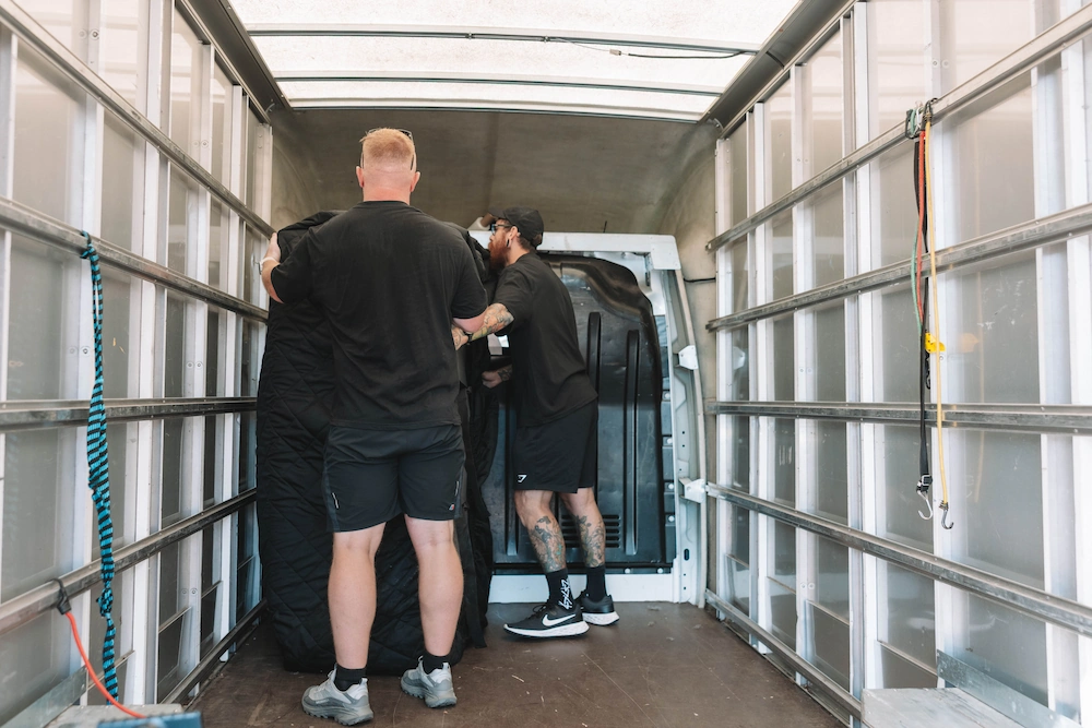 ShiftMate movers loading a wooden cabinet into a branded removals van